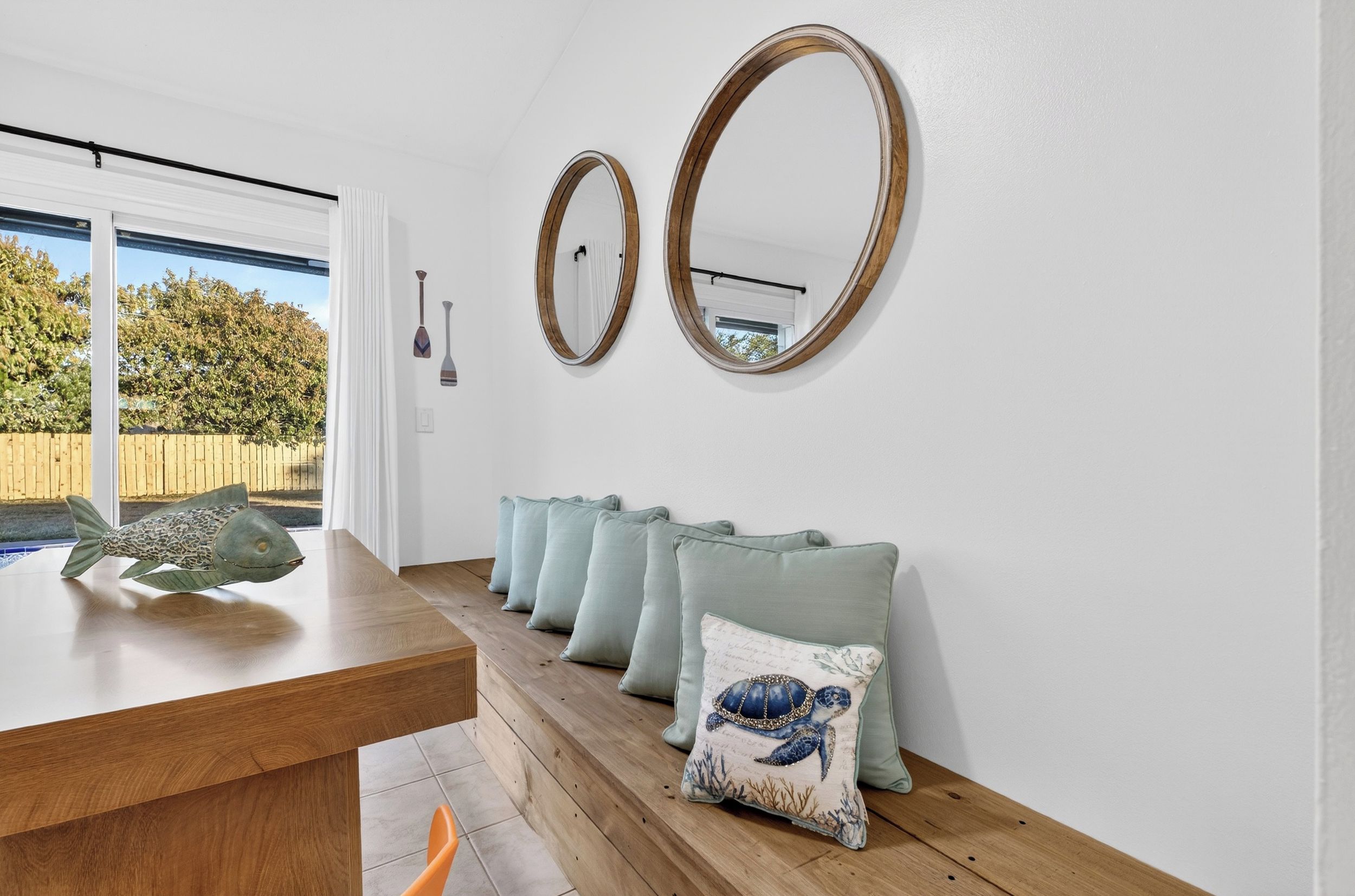 Una habitación con una mesa de comedor de madera, dos espejos colgados en la pared y una hilera de cojines verde claro con diseño de tortuga.