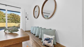 Una habitación con una mesa de comedor de madera, dos espejos colgados en la pared y una hilera de cojines verde claro con diseño de tortuga.