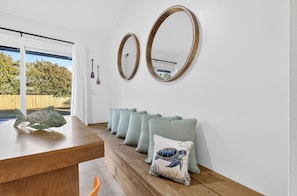 A room with a wooden dining table, two wall-mounted mirrors, and a row of light green cushions with a turtle design.