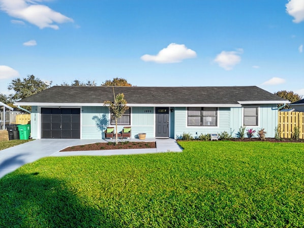A single-story house with a garage, a small front yard, and a tree.