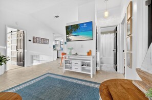 A spacious living area with a large painting of a beach scene, a white console table, and a blue rug.