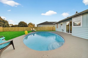 A residential backyard with a swimming pool, a wooden fence, and a house with a garage.