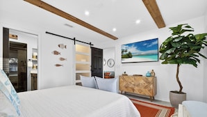 Ein Schlafzimmer mit Bett, Kleiderschrank, Spiegel, Pflanze und einem Bild an der Wand.