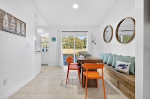 A dining area with a wooden table and orange chairs, a bench with cushions, and a view of a pool through a glass door.