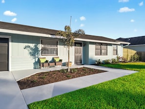 A residential house with a front porch, two chairs, a small tree, and a well-maintained lawn.