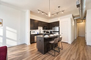 A modern kitchen with dark cabinetry, stainless steel appliances, and a central island with bar stools. - Design District 1BR | Reserved Parking | Sleeps 4 (Dallas)