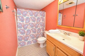 Ein Badezimmer mit einem waschsalonartigen Duschvorhang, einer Toilette, einem Waschbecken mit Spiegel darüber und Holzschränken.