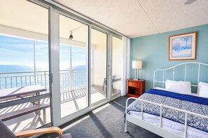 Ein Hotelzimmer mit Bett, Nachttisch, Tisch und Blick auf den Ozean.