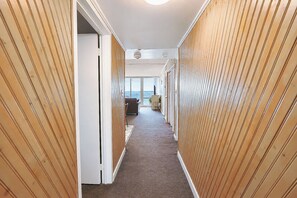 Een gang met houten lambrisering en vloerbedekking, die uitkomt in een kamer met uitzicht op de oceaan.