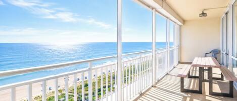 A balcony with a view of the ocean, a table, and chairs.