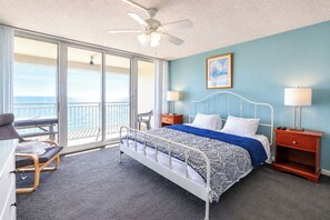 Een hotelkamer met een bed, een stoel, een nachtkastje, een lamp en uitzicht op de oceaan door een schuifdeur.