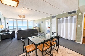 A modern living room with a glass dining table, comfortable seating, and a view of the ocean. - Carousel 1712 (Ocean City)