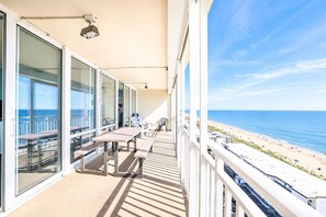 Ein Balkon mit Tisch und Stühlen mit Blick auf einen Strand und das Meer.