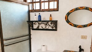 Un bagno con il water, un piccolo cestino, uno scaffale con articoli da toilette e uno specchio decorativo.