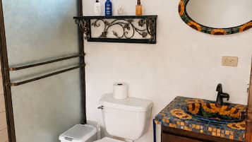 Ein Badezimmer mit Toilette, einem kleinen Mülleimer, einer Ablage für Toilettenartikel und einem dekorativen Spiegel.