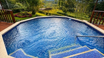 Ein Schwimmbad mit Blick auf eine üppige Landschaft, umgeben von einer Holzterrasse und Lichterketten.