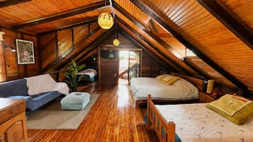 Ein gemütliches Schlafzimmer unter dem Dach mit Holzbalken, einem Sofa, einem Bett und einem Fernseher.