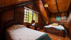 Una stanza con soffitto spiovente, pareti in legno, un letto con testiera, un comodino, uno specchio e una finestra che si affaccia sul verde.