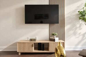 A modern living room with a flat-screen TV mounted on the wall, a wooden entertainment unit with a speaker, and a small plant on top. - Design District 2BR/2BA | Sleeps 6 | Parking (Dallas)