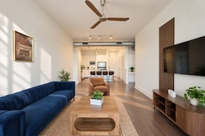 A modern living room with a blue sofa, a brown armchair, a wooden coffee table, and a TV on a wooden stand. - Modern 2BR/2BA | 3 Queen Beds | Design District (Dallas)