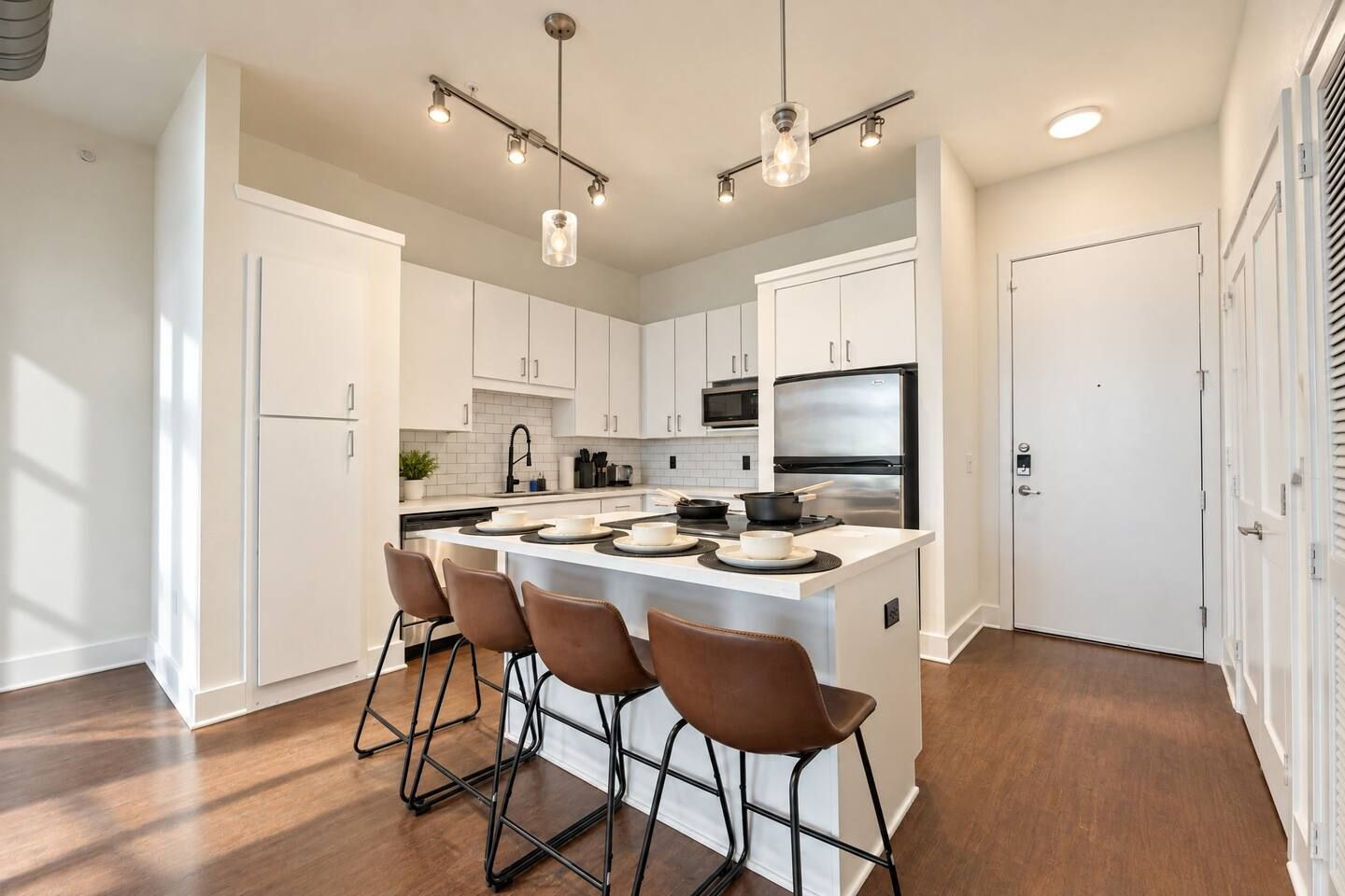 A modern kitchen with white cabinetry, a central island with bar stools, stainless steel appliances, and pendant lighting.