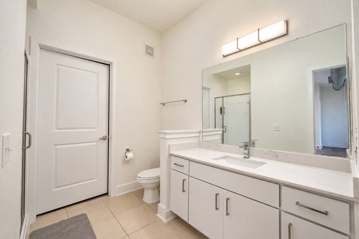 A bathroom with a toilet, sink, mirror, and cabinets.