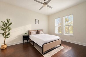 A bedroom with a bed, nightstand, potted plant, and two windows. - Brand-New 2BR/2BA | Reserved Parking | Sleeps 6 (Dallas)
