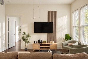Ein modernes Wohnzimmer mit einem wandmontierten Flachbildfernseher, einer Holz-Unterhaltungseinheit, einem Sofa, einem Sessel und einer Topfpflanze.