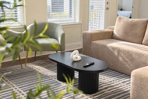 A living room with a sofa, armchair, and a black coffee table with a white object on it. - Brand-New 2BR/2BA | Reserved Parking | Sleeps 6 (Dallas)