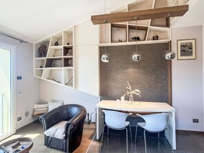 A modern dining area with a white table and chairs, a black leather chair, and a built-in shelving unit with various decorative items. - Borgo dei Fiori by Interhome (Magliolo)