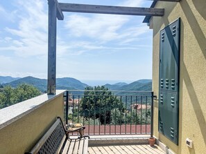 A balcony with a view of distant hills, a metal gate, and a table with a chair. - Borgo dei Fiori by Interhome (Magliolo)