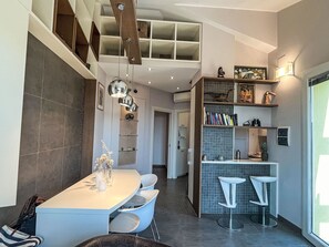 A modern kitchen with a dining area, featuring a central island, bar stools, and a staircase leading to an upper level. - Borgo dei Fiori by Interhome (Magliolo)