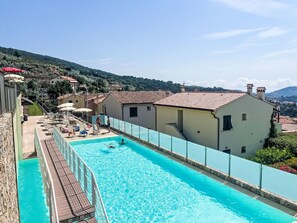 A swimming pool with a wooden deck, surrounded by buildings with red-tiled roofs. - Borgo dei Fiori by Interhome (Magliolo)