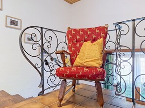 Een stoel met een kussen met een rood en geel patroon, op een betegelde vloer, met een metalen hekwerk op de achtergrond.