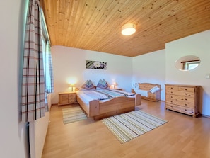 Ein Schlafzimmer mit Holzboden, einem Bett mit gemusterten Betttextilien, einem Nachttisch, einer Kommode und einem Spiegel.