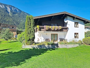 Ein modernes, zweistöckiges Haus mit Balkon, umgeben von einem gepflegten Rasen und einem Bergpanorama.
