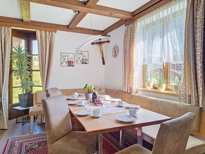 Ein Essbereich mit einem Holztisch, gedeckt für vier Personen, umgeben von gepolsterten Stühlen und Blick auf Grünflächen.