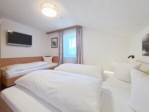 Une chambre d’hôtel avec deux lits, un téléviseur à écran plat fixé au mur, une fenêtre avec des rideaux et un tableau encadré au mur.