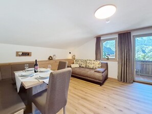 Un coin repas avec une table dressée pour deux personnes, un canapé et une fenêtre donnant sur un paysage montagneux.
