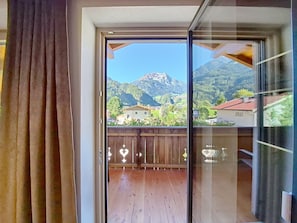 A room with a sliding glass door leading to a balcony with a wooden floor and a view of a mountain and houses. - Edelweiß by Interhome (Mayrhofen)
