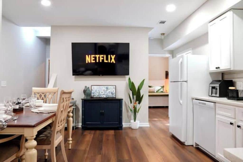 A modern kitchen with white cabinets, a black refrigerator, and a dining area with a wooden table and chairs.
