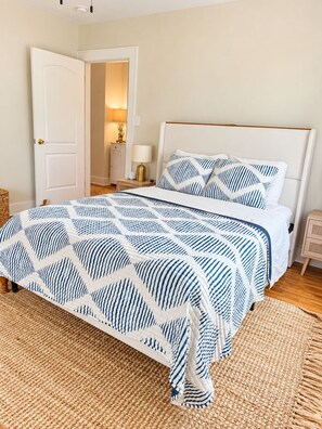 A bedroom with a bed, a nightstand, a lamp, and a door. - Cozy 2-bedroom house in beautiful Morehead City (Morehead City)