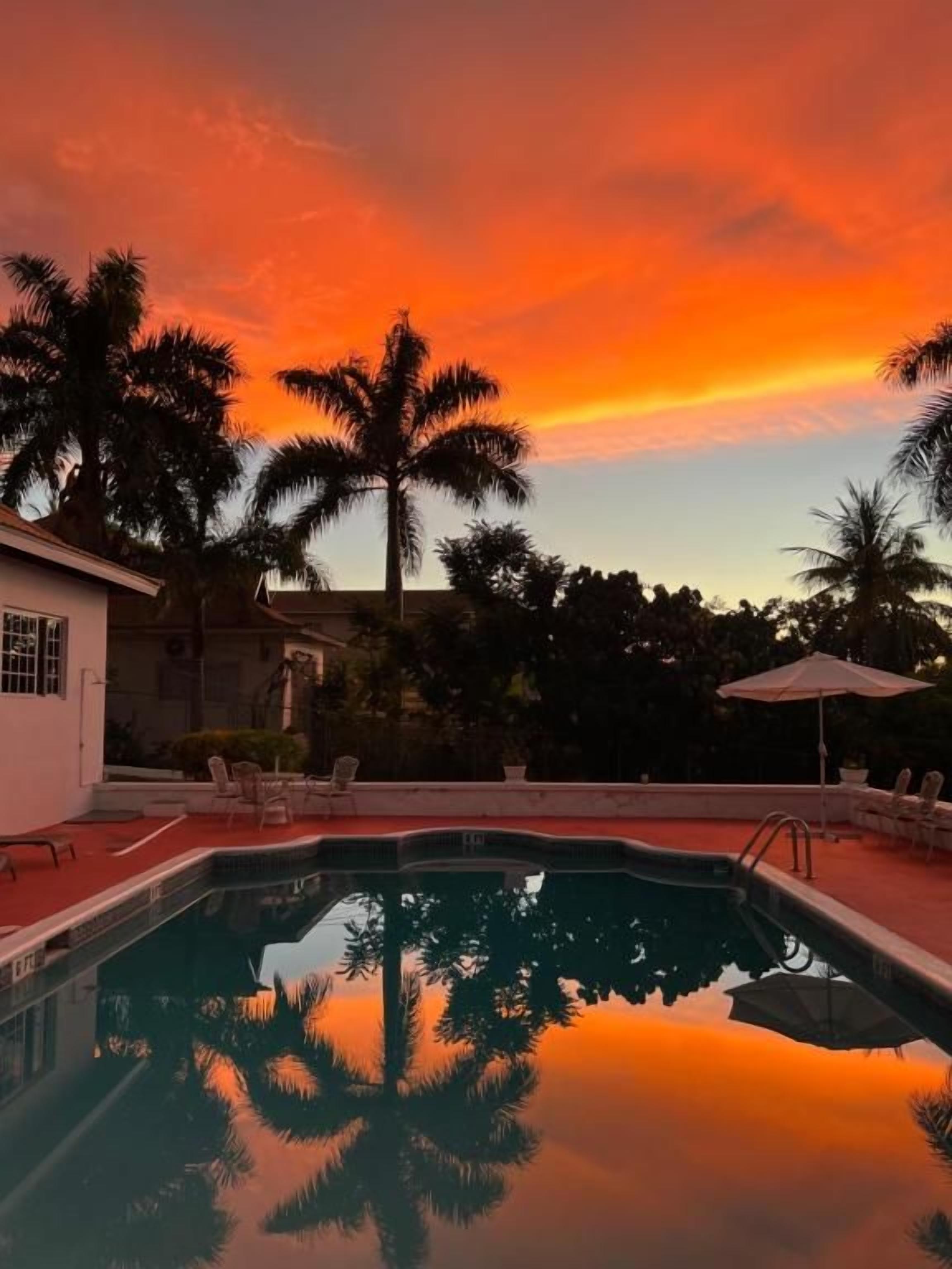 Une piscine bordée de palmiers et de chaises longues, entourée d’un bâtiment au toit rouge.
