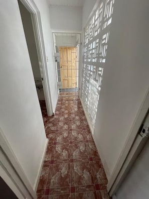 A narrow hallway with patterned flooring and a door at the end leading to a room with a wooden door.