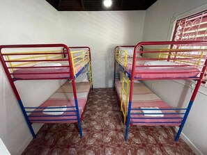 A room with bunk beds arranged in a row, a patterned floor, and a window with a metal grille.