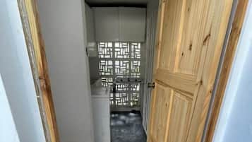 Un couloir étroit, avec une porte en bois sur la droite et une porte blanche sur la gauche.
