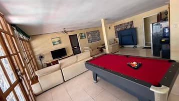 Une table de billard dans une pièce où se trouvent un canapé et un téléviseur.
