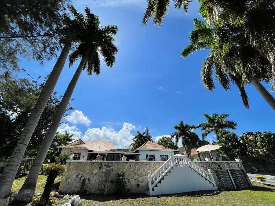 A house with a stone facade, a white staircase, and palm trees in the background.