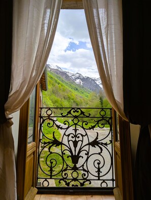 Finestra amb vista a un paisatge de muntanya, cortines i una reixa de ferro decorativa.