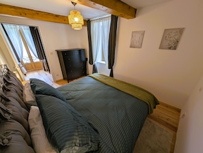 Un dormitori amb un llit, una petjaca, una finestra amb cortines i una lluminària penjant.